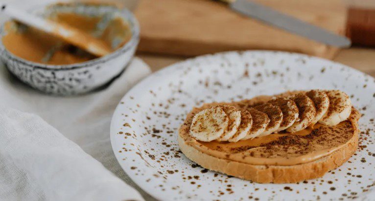 På vår första årsdag kom Clay med frukost på sängen – bacon, kaneltoast och en hemlig utflykt. Jag trodde att han äntligen var redo att lämna sitt förflutna bakom sig. Men någonstans mellan majsfälten och de tysta blickarna insåg jag att den här resan inte handlade om mig. När jag vaknade kände jag doften av bacon – knaprigt, rökigt, rikt – och något sött, som om kanel smälte på varm toast. Det omslöt mig som en filt. I ett ögonblick trodde jag att jag drömde. Man får inte sådan frukost utan anledning. Inte en vanlig onsdag. Inte utan något bakom. Han tog med mig på en överraskningsresa för vår årsdag, men när jag klev ur bilen insåg jag att det inte var för min skull. Jag öppnade ögonen och kisade mot det tidiga solljuset som föll genom persiennerna. Och där stod han. Clay stod vid fotänden av sängen, barfota, håret rufsigt efter sömnen, med en bricka i händerna. På brickan: två skivor kaneltoast, staplade som gyllene tegelstenar, en hög bacon och en vit mugg – min favoritmugg, den med den spruckna kanten. Han log med det där sällsynta leendet, knappt märkbart på läpparna, men det värmde upp hela rummet. ”Grattis på årsdagen,” sa han mjukt och satte ner brickan i mitt knä, som om den var något dyrbart. Jag tittade på brickan, sedan på honom. ”Du glömde inte?” Han ryckte på axlarna som om det inte var något. Men det var det. Det betydde allt. Det var vårt första år tillsammans. Bara ett år – men för mig var det mer än ett datum i kalendern. Det var ett bevis. Bevis på att vi tagit oss igenom de svåra månaderna, grälen om ingenting, det försiktiga lärandet om varandra. Bevis på att jag inte bara var någon i förbifarten. Clay var inte typen för stora gester. Han hade tidigt sagt att hans tidigare förhållande hade krossat mer än bara hans hjärta. Han tog med mig på en överraskningsresa för vår årsdag, men när jag klev ur bilen insåg jag att det inte var för min skull. Sedan dess gjorde löften honom nervös. När han pratade om framtiden blev han tyst. Han hade aldrig sagt: ”Jag älskar dig.” Inte en enda gång. Och inte jag heller. Jag hade väntat. Kanske var det stolthet. Kanske rädsla. Kanske båda. Men när han gav mig brickan, satte sig bredvid mig i sängen och såg på mig som om han höll andan, fick jag en klump i halsen. ”Jag har gjort planer,” sa han hest. ”En roadtrip. Bara vi. En hel helg. Inga telefoner.” Jag blinkade. ”Har du fixat allt det här?” Han nickade, ögonen klara. ”Du kommer att älska det. På riktigt.” Och i det ögonblicket, medan toasten fortfarande ångade och doften av bacon fyllde rummet, trodde jag honom. Jag ville också tro det. Kanske var det här början på allt. Senare på morgonen körde vi ut på motorvägen, kaffemuggarna fortfarande varma i hållarna, Clays favoritmusik dånade ur högtalarna. Himlen sträckte sig blå och vid som ett nytvättat lakan. Majsfälten i Iowa bredde ut sig på båda sidor som gyllene mattor som svajade i fartvinden. Clay körde med en hand på ratten och trummade med den andra till rytmen av en gammal rockklassiker. Varje kilometer sneglade han på mig och log. ”Jag tänker inte säga vart vi ska,” sa han för tredje gången. Jag skrattade och lutade mig bakåt. ”Du är verkligen hemlighetsfull, va?” Han flinade. ”Vänta bara. Du får se. Lita på mig.” Vi körde förbi slingrande floder, klippor som liknade sagor och gamla lador med flagande färg och skeva tak – som om de var trötta på att stå upp. Clay pekade ständigt på saker. ”Kolla ladan!”, sa han. ”Hur den lutar? Som om den ska falla men ändå håller sig kvar.” Jag tog upp mobilen. ”Vill du att jag tar ett foto?” ”Ja, ja. Men få med kullen bakom också. Ljuset är perfekt.” Jag tog bilden, även om vinkeln inte blev bra. Sedan passerade vi ett fält med vilda blommor. Lila och gula fläckar dansade i vinden. Jag log. ”Det här påminner mig om mormors trädgård. Hon hade sådana vid verandan.” Clays ansikte förändrades. Inte argt, men... irriterat. ”Det var inte det jag menade,” sa han. ”Glöm blommorna. Titta på kullen. På ljuset.” Jag blinkade. ”Okej… visst.” Han vände sig mot vägen igen och blev tyst. Och jag satt där, osäker. Bröstet kändes trångt, som om ett rep dragits runt det. Det handlade inte bara om blommorna. Det var hur han sa det – som om jag inte förstod. Som om jag gjorde fel. Men jag sa till mig själv: han försöker. Han har planerat den här resan. Gjort spellistan. Lagt frukost. Det här är hans sätt att älska. Kanske ser det annorlunda ut än mitt, men det är något. Han tog med mig på en överraskningsresa för vår årsdag, men när jag klev ur bilen insåg jag att det inte var för min skull. Jag tittade ut genom fönstret och såg milen passera. Men inom mig viskade en röst: varför känns det som ett prov jag inte visste att jag skulle ta? Framåt eftermiddagen svängde vi in på en grusväg vid en nationalpark. Däcken knastrade över stenarna, Clay parkerade. Höga träd kantade parkeringen, deras grenar rörde sig mjukt i vinden. Jag vevade ner rutan och andades in doften av tall och fuktig jord. Längre bort hörde jag ett svagt brus av vatten – stilla men tydligt, som om naturen viskade en hemlighet. Clay var redan ute innan jag lossat bältet. Han gick snabbt framför mig, nästan otålig. ”Kom nu,” ropade han. ”Det här är det bästa.” Jag följde honom längs en skuggig stig. Fåglar sjöng i träden. Marken var fuktig och ojämn, och solljuset bröt ibland genom trädkronorna och kastade gyllene fläckar på jorden. Vi rundade en sväng och då såg jag det. Vattenfallet var inte stort – kanske tre meter – men det var vackert. Vattnet föll över mörka stenar ner i en grund pool. Dimmiga droppar dansade i luften, fångade av solljuset, silvriga och mjuka, som rök ur en dröm. Clay stannade och såg på det, som om det betydde något. Jag såg också. Och någonstans i bröstet väcktes ett minne. ”Jag tror jag har varit här förut,” sa jag tyst. ”När jag var liten. Mina föräldrar tog med oss hit och tältade. Jag tror att det var här.” Clay vände sig om. Hans ansikte förändrades. Värmen i ögonen slocknade, som om någon slog av en strömbrytare. ”Du har redan sett det här?” frågade han stilla. ”Ja, men…” började jag. Han skakade snabbt på huvudet och vände bort blicken. ”Så skulle det inte vara.” Jag blinkade. ”Vad menar du?” Men han svarade inte. Han gick redan tillbaka mot bilen. På motellet i närheten sa han inte ett ord. Han släppte ner våra väskor på golvet, stängde dörren och satte sig på sängkanten med ryggen mot mig. Jag stod där, mållös. Hade jag förstört något? Med hjärtat bultande gick jag ut. Jag behövde luft. Utrymme. Och då såg jag det. Inristat i barken på ett gammalt träd vid skogskanten – ett hjärta. Där i: Clay och Megan. Han tog med mig på en överraskningsresa för vår årsdag, men när jag klev ur bilen insåg jag att det inte var för min skull. Världen vände sig. Megan. Namnet han sagt tillhörde det förflutna. Plötsligt föll allt på plats. Jag stod vid fönstret, armarna i kors, stirrade på den tomma parkeringen. En fjäril slog mot glaset. Luften på motellet kändes tung, som om den inte rört sig på åratal. Bakom mig låg Clay på sängen, händerna vikta över bröstet, stirrade upp i taket som om det försökte säga honom något. ”Det handlade inte om mig, eller hur?” viskade jag. Min röst kändes liten, som en sten i en djup brunn. Clay svarade inte direkt. Han satte sig långsamt upp, armbågarna på knäna, stirrade på den slitna mattan. Han såg ut som om han höll något inne, som om bröstet var fullt av rök och han inte fick luft. ”Det var menat för oss,” sa han till slut. ”En nystart.” Han gnuggade händerna mot varandra och såg mig fortfarande inte i ögonen. ”Men ja… jag har varit här förut. Med henne.” Mitt hjärta sjönk. Jag behövde inte fråga vem hon var. ”Jag ville inte att du skulle få veta det så här,” viskade han. ”Det var en av de bästa helgerna i mitt liv. Jag tänkte, om jag kom tillbaka – med dig – kanske jag kunde skriva om det. Skapa nya minnen. Byta ut de gamla.” Han svalde. ”Jag visste inte att allt skulle komma tillbaka så fort.” Jag sa inget. Jag kunde inte. Tankarna var en röra, känslorna en knut jag inte kunde reda ut. ”Älskar du henne fortfarande?” frågade jag. Orden kom ut som om jag frågade om vädret. Clays käke spändes. Han öppnade munnen, stängde den igen. Andades djupt. ”Jag vet inte,” sa han. ”Jag tror inte det. Men kanske… kanske saknar jag den jag var när jag var med henne. Den versionen av mig kändes lättare. Gladare.” Och då insåg jag det. Den här resan – den var inte riktigt för oss. Den var för ett spöke. För någon han en gång varit. Och plötsligt var jag inte arg på henne. Jag var sårad, för jag var inte ens huvudpersonen i mitt eget kärlekshistoria. ”Jag behöver dig här,” viskade jag. ”Inte där. Inte med henne.” Han nickade. Men såg mig fortfarande inte i ögonen. Orden kom ut innan jag hann stoppa dem. ”Jag älskar dig.” Han tittade förvånat upp. Men han sa det inte tillbaka. Tårarna steg. Jag vände mig om, tog min tröja och gick ut. Luften var kallare än jag väntat mig. Men jag kunde åtminstone andas. När jag nådde parkeringen färgades himlen ljusblå, nästan lila. Det doftade av tall och damm. Jag stod stilla, armarna i kors. Vinden drog lätt i mina ärmar. Jag torkade mig över ögonen, trots att tårarna redan torkat. Bröstet kändes fortfarande trångt, som om det hölls ihop av ett snöre. Varför sa jag det först? Varför nu? Orden hade fallit – tunga och verkliga – och nu svävade de mellan oss, obesvarade. Jag skulle just gå vidare när jag hörde dörren slå igen. Han tog med mig på en överraskningsresa för vår årsdag, men när jag klev ur bilen insåg jag att det inte var för min skull. ”Vänta!” Clays röst sprack som glas. Jag vände mig om, förvånad. Han sprang barfota mot mig, stegen snabba och klumpiga över gruset, fortfarande i jeans och skrynklig T-shirt. Inga skor. Det spelade ingen roll vem som såg. Hans hår var rufsigt, ansiktet rött. Han grep tag i min hand som om han behövde den för att kunna andas. ”Jag var dum,” flämtade han. ”Jag trodde att jag kunde täcka gammal smärta med något nytt. Att om jag gick samma steg, kunde jag lura mig själv att jag gått vidare.” Han kramade min hand hårdare. ”Men du hade rätt. Det här handlar inte om henne. Det borde det aldrig gjort. Du är ingen ersättning. Du är den.” Han svalde. ”Jag älskar dig också.” Sedan tog han ett steg tillbaka och ropade – högt nog att eka mot motellets vägg: ”Jag älskar henne!” Ett fönster gnisslade upp. Någon tittade yrvaket ut. En hund skällde. Men Clay brydde sig inte. Han såg på mig och sa igen, tystare: ”Jag älskar dig.” Hans panna nuddade min, varm och stadig. Jag slöt ögonen och kände det – verkligen kände det. Det här var ingen historia från det förflutna. Inget spöke från en helg med någon annan. Det här var vårt. Vilka spöken vi än bar på, fick de följa med. Men de skulle alltid stanna bakom oss. För det här – det skrevs nu. Levende. Varmt. Äkta. Och för första gången trodde jag verkligen på honom.